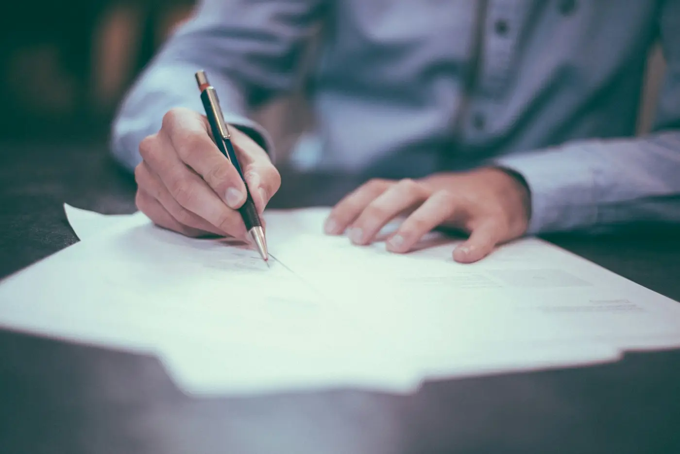 A hand signing a paper document with a pen